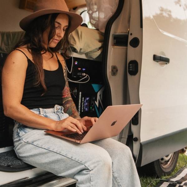 A traveller using a laptop beside a van fitted with PowerBoss